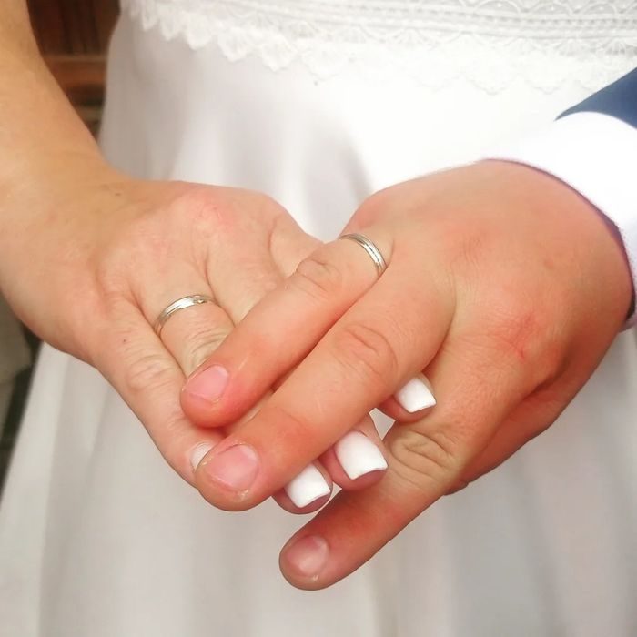 Mano de novia y mano de novio entrelazadas, ambas llevan anillos de boda.